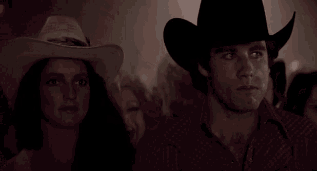 a man and a woman wearing cowboy hats are standing next to each other in a crowd .