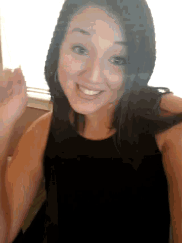 a woman in a black top is smiling and waving her hand