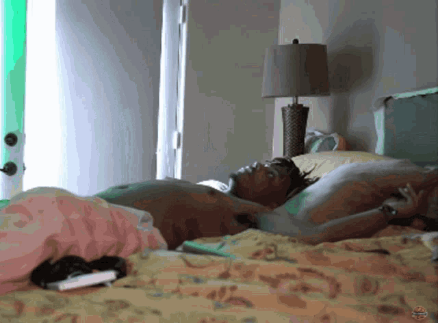 a shirtless man laying on a bed with a lamp