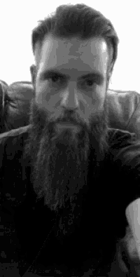 a man with a beard is sitting on a couch taking a selfie .