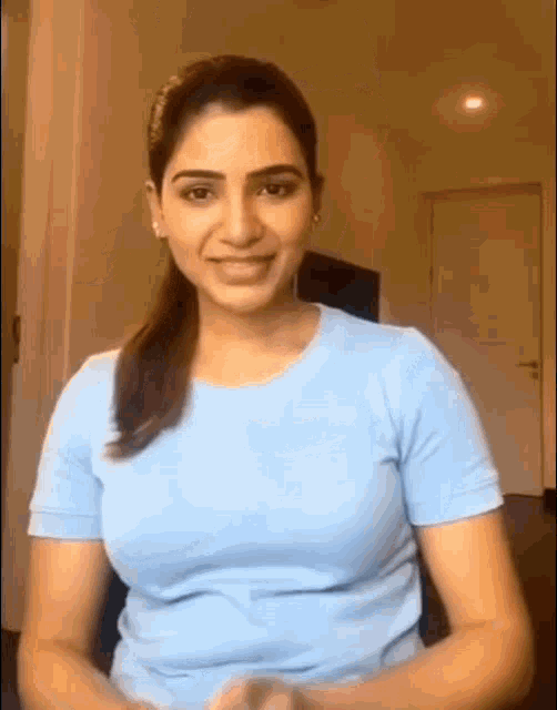 a woman in a blue t-shirt is sitting in a chair and smiling at the camera .
