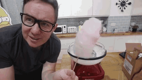 a man wearing glasses is making cotton candy in a machine .