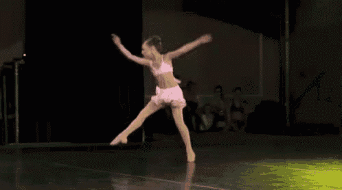 a young girl in a pink dress is jumping in the air on a stage .