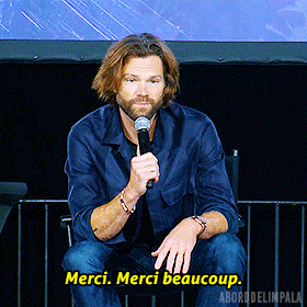 a man sitting in front of a microphone with the words merci merci beaucoup below him