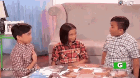 three children are sitting at a table with a green g on the bottom of the screen