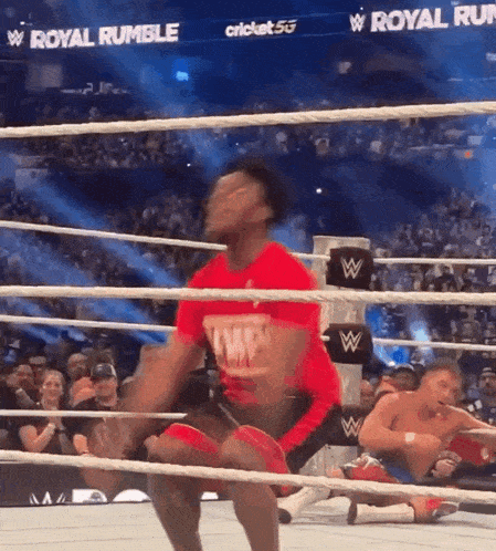 a man in a red shirt is jumping in a wrestling ring at a royal rumble event