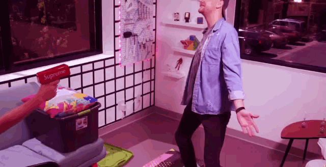 a man is standing in a living room with a supreme box in his hand