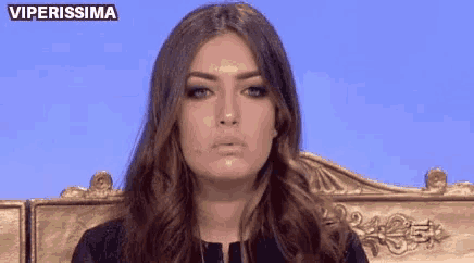 a woman with long hair is sitting on a gold chair and making a face .