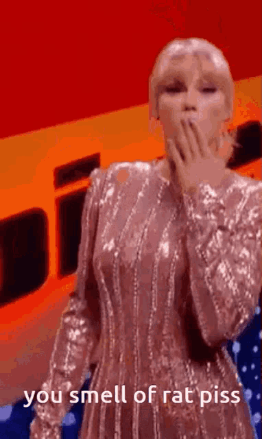 a woman in a sequined dress is covering her mouth with her hand while standing on a stage .