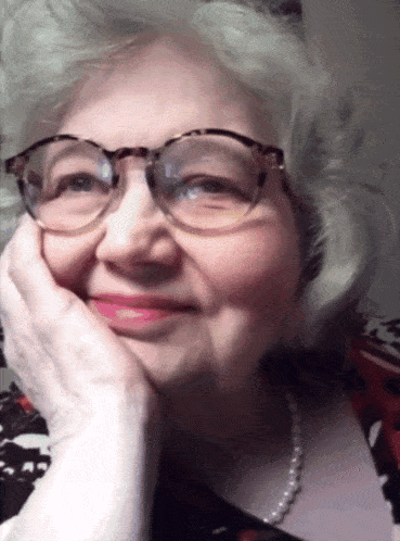 a woman wearing glasses and a pearl necklace smiles