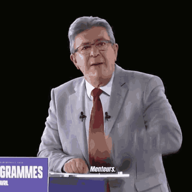 a man in a suit and tie stands in front of a sign that says grammes