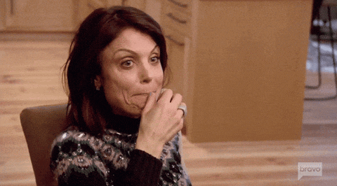 a woman with a ring on her finger is sitting in a chair with her hand on her mouth .