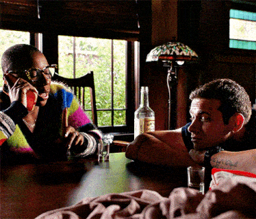a man and a woman sit at a table with a bottle of vodka on the table