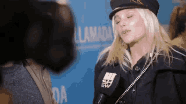 a woman wearing a hat is talking into a microphone while standing in front of a blue sign that says llamada
