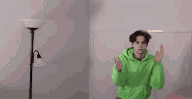 a man in a green hoodie is standing in a room with his hands folded .