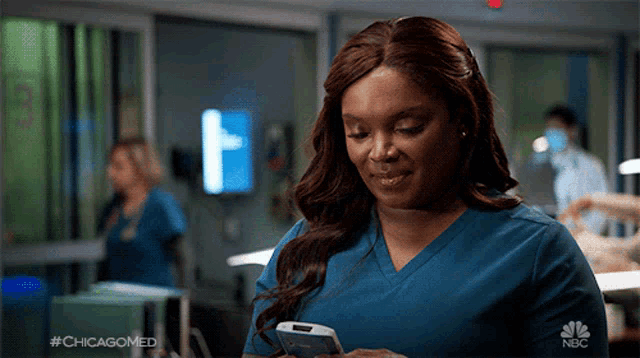 a woman in a blue scrub is looking at her phone with #chicagomed on the bottom