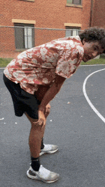 a man wearing a floral shirt and black shorts is kneeling down on a basketball court
