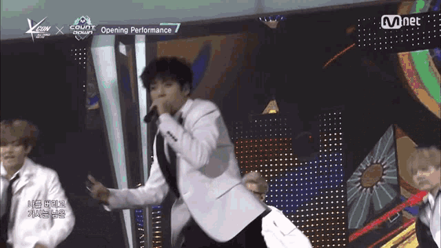 a man in a white suit is singing into a microphone with the words opening performance behind him