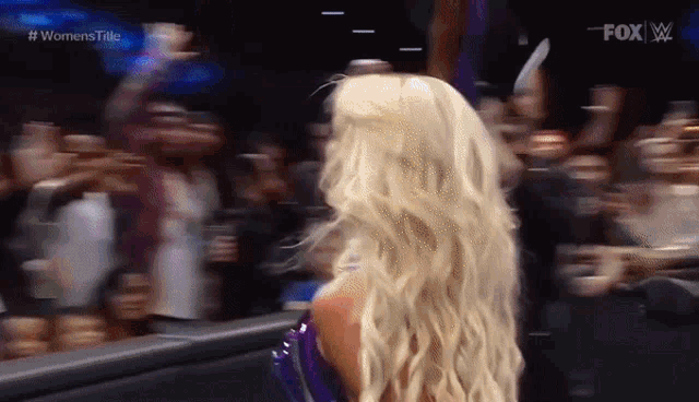a woman with blonde hair is standing in front of a crowd at a women 's wrestling event