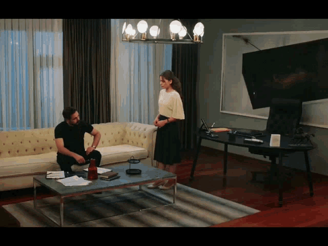 a man sits on a couch while a woman stands next to him in a living room