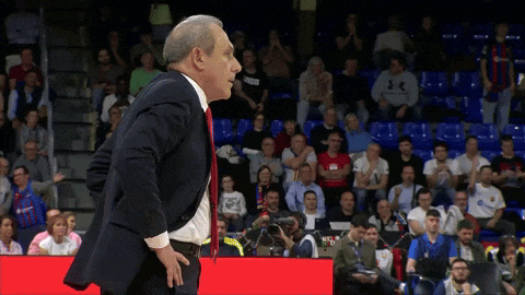a man in a suit and red tie stands in front of a crowd watching a game