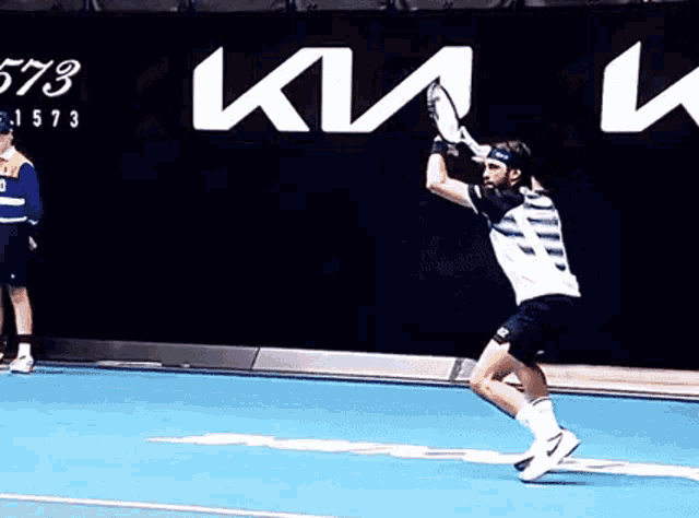 a man is swinging a tennis racquet on a court in front of a kia ad