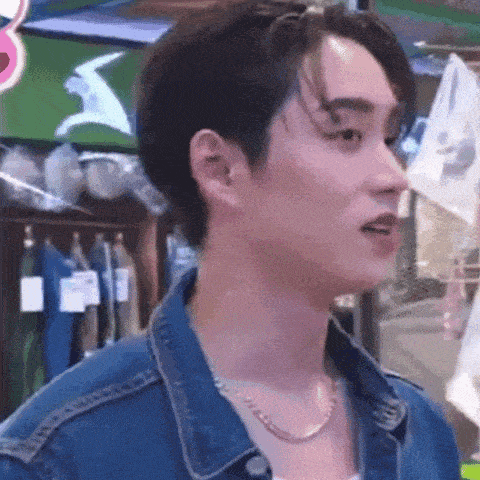 a young man wearing a denim jacket and a necklace is standing in a store .