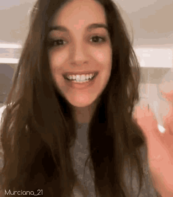 a woman with long hair is smiling and waving her hand .