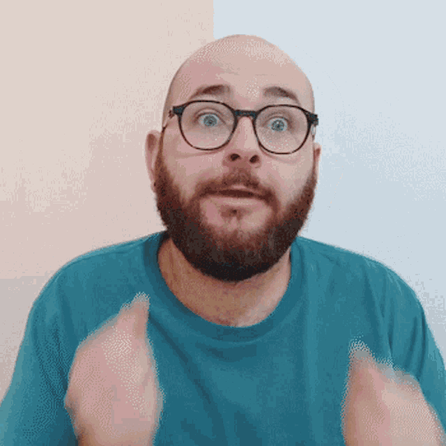 a bald man with a beard wearing glasses and a blue shirt is making a surprised face