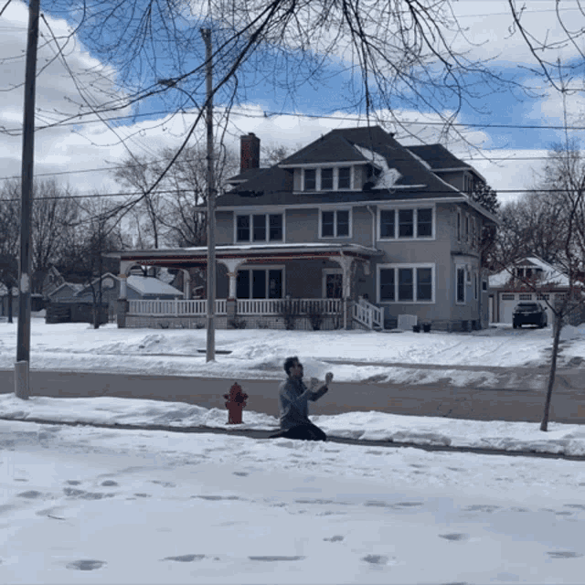 a man is throwing a snowball in front of a house with a fire hydrant
