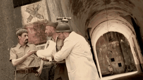 a man in a white coat is helping a man in a helmet carry something
