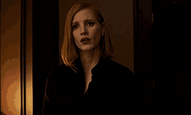 a woman in a black shirt is standing in a dark room looking at the camera .