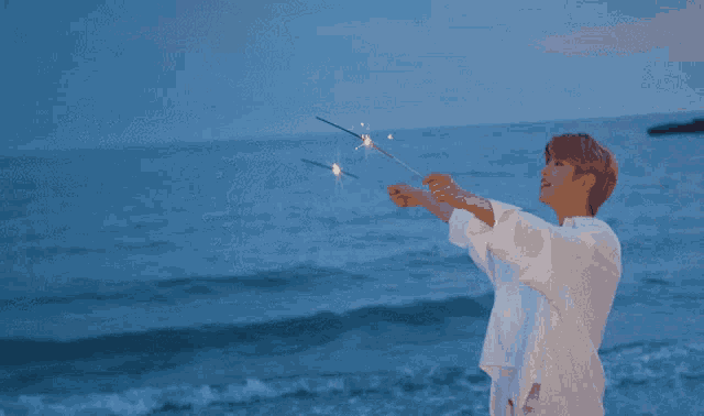 a man is holding a sparkler in front of the ocean