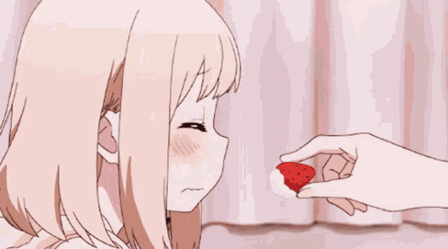 a person is holding a strawberry in front of a girl 's face