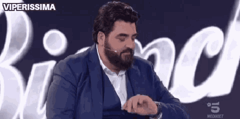 a man with a beard is sitting in front of a microphone and looking at his watch .