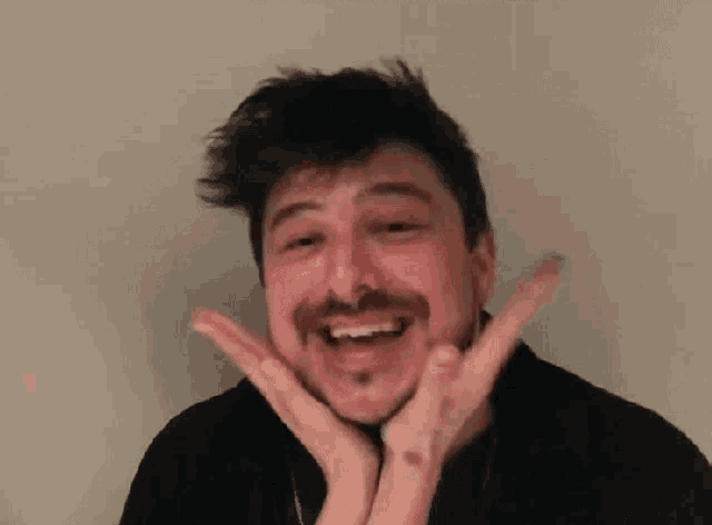 a man with a beard and mustache is making a funny face with his hands on his face .