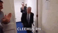 a man in a suit and tie is walking through a doorway while two other men applaud .