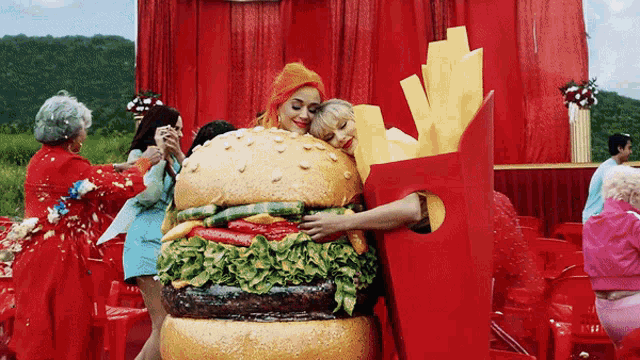 a woman in a hamburger costume is hugging a woman in a french fries costume