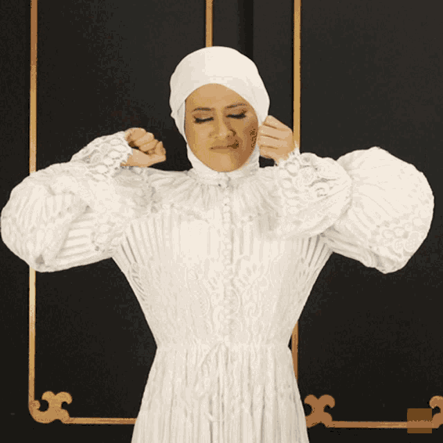 a woman in a white dress and hijab covering her face with her hands