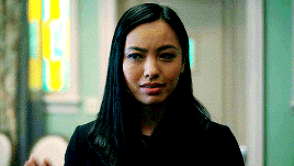 a woman with long black hair is standing in front of a stained glass window in a room .