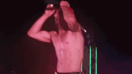a man without a shirt is singing into a microphone on stage .