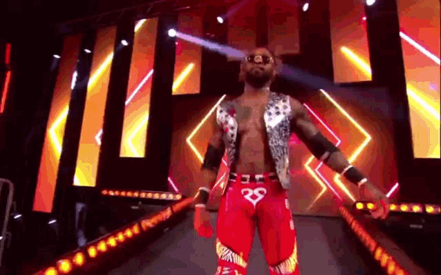 a wrestler is standing on a stage in front of a large screen holding a bat .