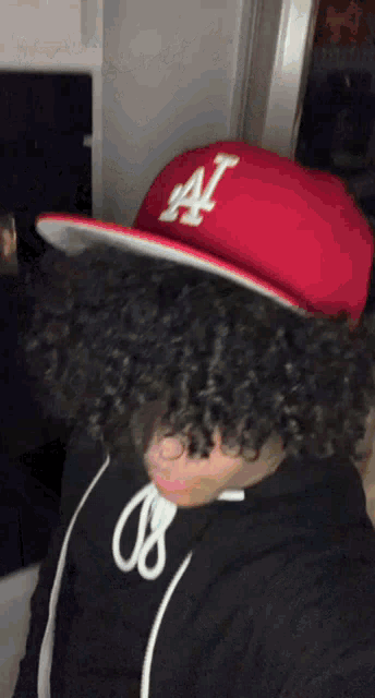 a person with curly hair wearing a red hat with the letter a on it