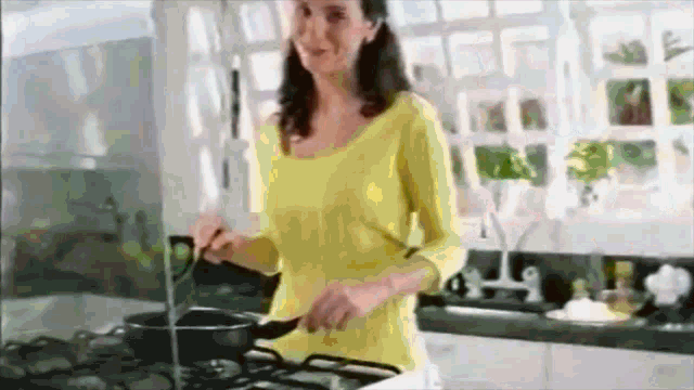a woman in a yellow shirt is cooking on a stove top