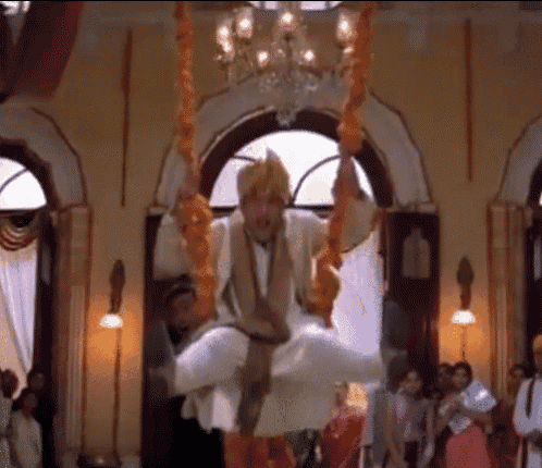 a man in a turban is sitting on a swing in a room with other people .