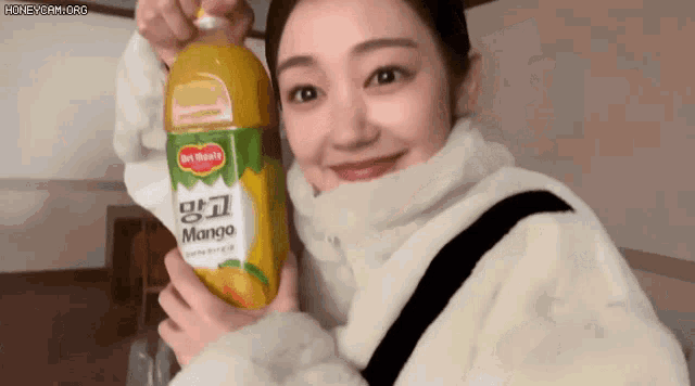 a woman is holding a bottle of mango juice in her hands