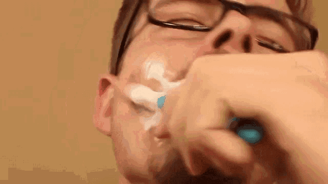 a man with glasses is brushing his teeth with a toothbrush and toothpaste .
