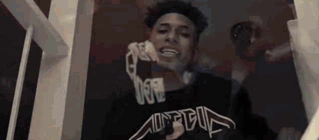 a young man is standing in front of a mirror wearing a black shirt that says ' a ' on it .