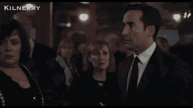 a man in a suit and tie stands in front of a crowd and says " il a dit "