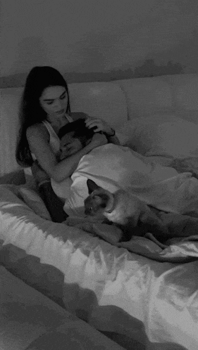 a black and white photo of a woman laying on a bed with a man and a dog